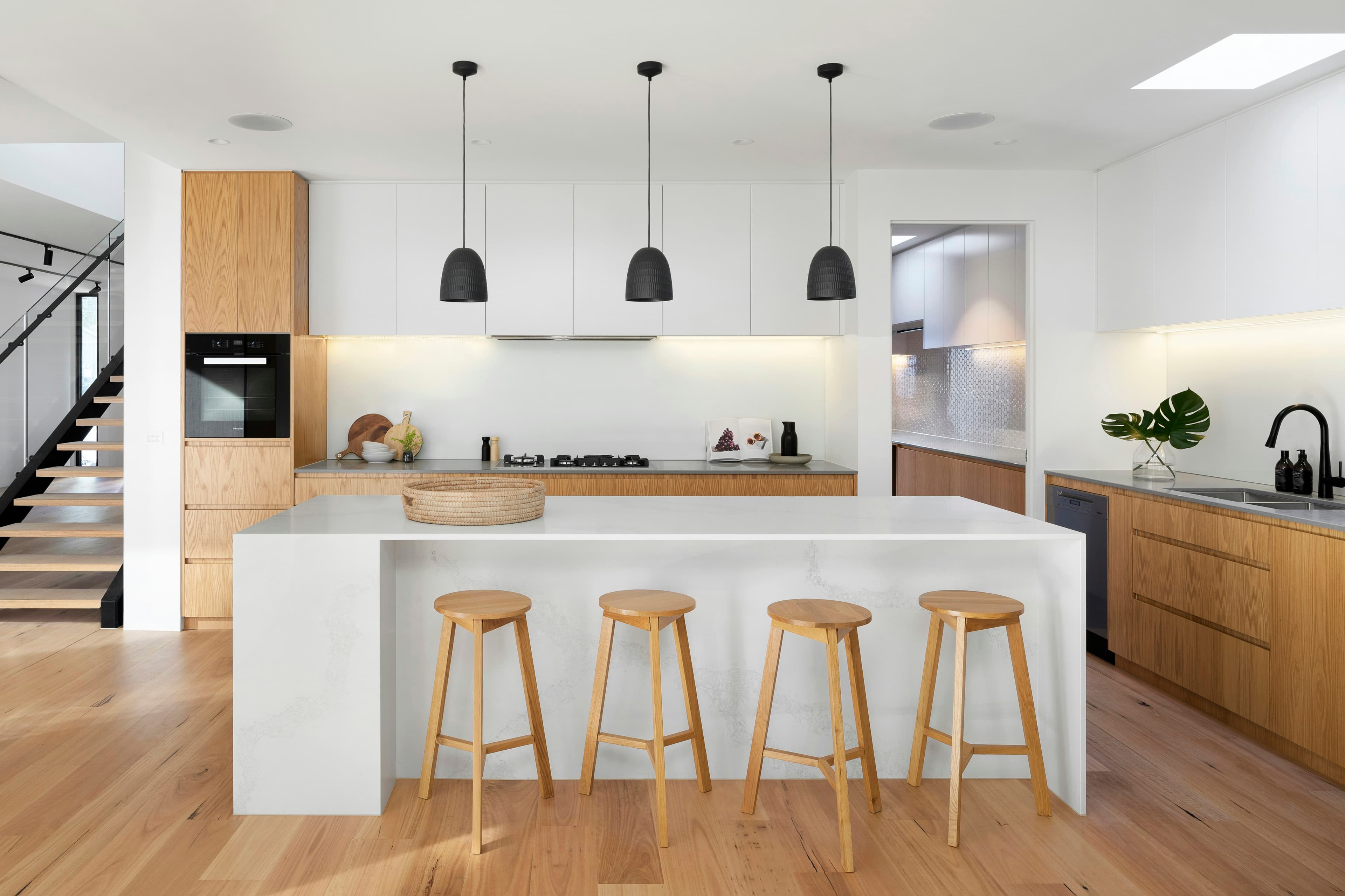 Cocina con gabinetes de roble, isla de cuarzo blanco y bancos de madera
